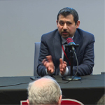A person seated at a table speaks into a microphone