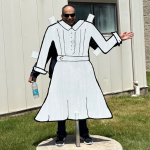 A person poses behind a 2-dimensional sculpture of a dress