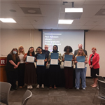 A group of people poses, smiling, with five people in the middle holding certificates.