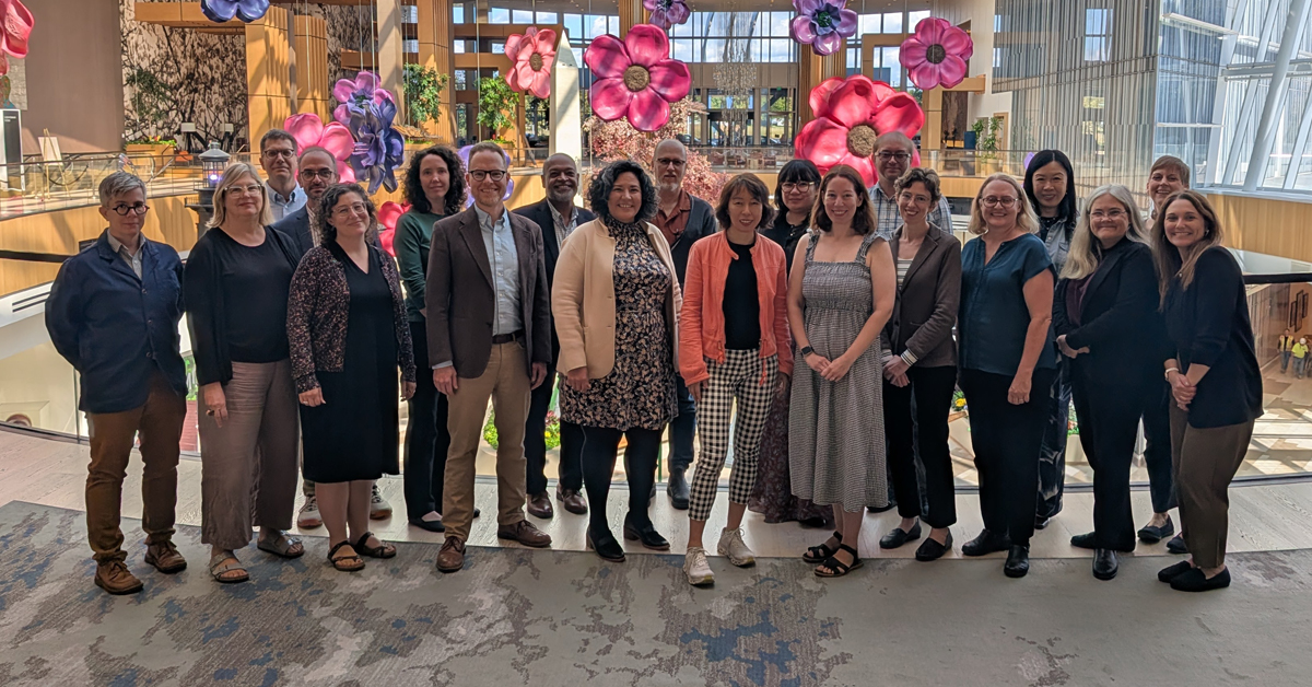 A large group of adults poses, smiling, in a brightly lit conference center.