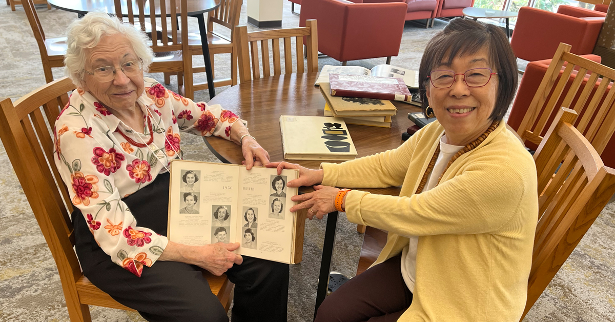 Two people sit at a table, smiling and holding an open yearbook.