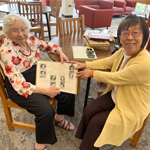 Two people seated at a table smile at the camera holding an open yearbook