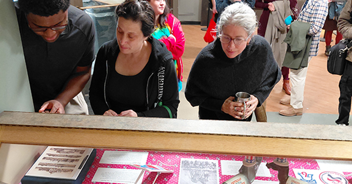 Three people are looking down at objects in a display case.